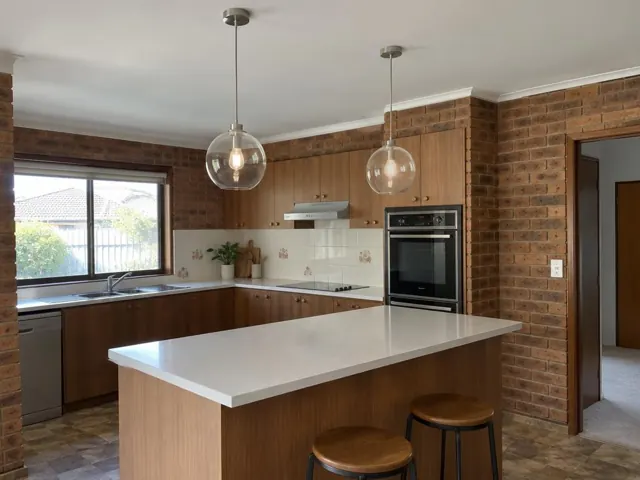 Kitchen with two glass pendant lights above a white island, wood cabinets and brick walls in Wyoming