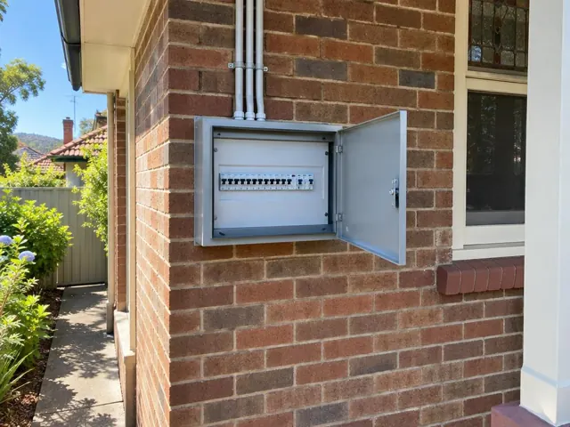 Open exterior switchboard on a brick house wall beside a window in Gosford